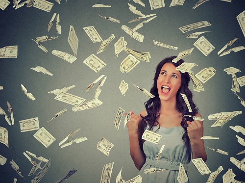 Woman with long brown hair standing under money falling from the sky
